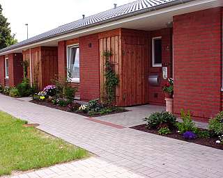 Eingang mit Holzverkleidung und bunten Blumenbeeten.